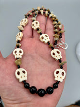 Load image into Gallery viewer, This skully necklace is full of neutral tones and is adorned with natural black obsidian and bamboo chips, as well as small glass beads. It has a unique design that creates a striking silhouette across the wearer's neck. An ideal statement piece for bold fashion enthusiasts. Measurements: Necklace - 19 1/4"