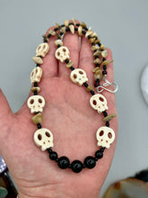 Load image into Gallery viewer, This skully necklace is full of neutral tones and is adorned with natural black obsidian and bamboo chips, as well as small glass beads. It has a unique design that creates a striking silhouette across the wearer's neck. An ideal statement piece for bold fashion enthusiasts. Measurements: Necklace - 19 1/4"