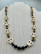 Load image into Gallery viewer, This skully necklace is full of neutral tones and is adorned with natural black obsidian and bamboo chips, as well as small glass beads. It has a unique design that creates a striking silhouette across the wearer's neck. An ideal statement piece for bold fashion enthusiasts. Measurements: Necklace - 19 1/4"