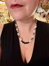 Load image into Gallery viewer, This skully necklace is full of neutral tones and is adorned with natural black obsidian and bamboo chips, as well as small glass beads. It has a unique design that creates a striking silhouette across the wearer's neck. An ideal statement piece for bold fashion enthusiasts. Measurements: Necklace - 19 1/4"