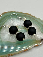 Load image into Gallery viewer, These flat matte black glass bead earrings are perfect for creating a cocktail chic ensemble. With a round shape and silver plated floral bead, this timeless piece is ideal for special occasions such as weddings. Its minimalist look exudes effortless elegance. Measurements: 1 1/4” in length