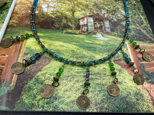 Load image into Gallery viewer, This necklace features vivid green and blue glass beading and a yin yang brass octagon charm. Each side of the charm is distinct, creating a two-in-one look. The look is further enhanced with the addition of rectangular rainbow hematite beads for added visual complexity. Double-hole flat matte gold beads keep the collar shape and add to the necklace's elegant draping when worn.  Measurements:    Necklace is 23” in length