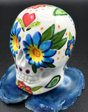Load image into Gallery viewer, Inspired by nature, this ceramic skull statuette is full of vibrant color and intricate details. The primary color is white with Multi-color floral motifs that are painted across the skull, along with hearts and leaves and lively colorful accents around the entire skull.