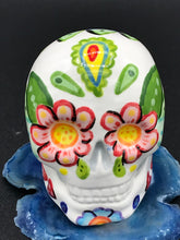 Load image into Gallery viewer, Inspired by nature, this ceramic skull statuette is full of vibrant color and intricate details that I hand painted. The primary color is white with multi-color floral motifs that are painted across the skull, along with hearts and leaves and lively colorful accents around the entire skull.