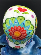 Load image into Gallery viewer, Inspired by nature, this ceramic skull statuette is full of vibrant color and intricate details that I hand painted. The primary color is white with multi-color floral motifs that are painted across the skull, along with hearts and leaves and lively colorful accents around the entire skull.