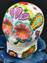 Load image into Gallery viewer, Inspired by nature, this ceramic skull statuette is full of vibrant color and intricate details that I hand painted. The primary color is white with multi-color floral motifs that are painted across the skull, along with hearts and leaves and lively colorful accents around the entire skull.