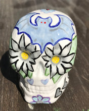Load image into Gallery viewer, This ceramic skull art is a unique and eye-catching combination of bright colors and dark tones. It features two bat silhouettes and flowers in warm colors like red, yellow, and green, as well as medium gray and royal blue. Its vibrant red eyes give the piece an inviting touch. Perfect for a mini goth witchy altar, this figurine is sure to stand out. Measurements: H 2 3/4” x W 2” x D 2”