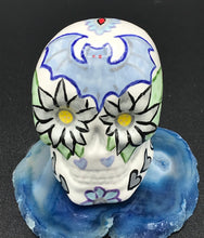 Load image into Gallery viewer, This ceramic skull art is a unique and eye-catching combination of bright colors and dark tones. It features two bat silhouettes and flowers in warm colors like red, yellow, and green, as well as medium gray and royal blue. Its vibrant red eyes give the piece an inviting touch. Perfect for a mini goth witchy altar, this figurine is sure to stand out. Measurements: H 2 3/4” x W 2” x D 2”