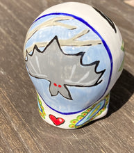 Load image into Gallery viewer, This Bat Lovers Ceramic Skull Art is a unique addition to any dark gothic collection. Featuring a mini batty with bright red eyes and outlined in royal blue, accented with white lines to highlight its small bones and an additional bat with vibrant red eyes on the opposite side. Enjoy the playful contrast of warm tones and a darker theme in this eye-catching figurine. Measurements: H 2 3/4” x W 2” x D 2”