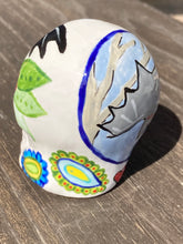 Load image into Gallery viewer, This Bat Lovers Ceramic Skull Art is a unique addition to any dark gothic collection. Featuring a mini batty with bright red eyes and outlined in royal blue, accented with white lines to highlight its small bones and an additional bat with vibrant red eyes on the opposite side. Enjoy the playful contrast of warm tones and a darker theme in this eye-catching figurine. Measurements: H 2 3/4” x W 2” x D 2”