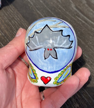 Load image into Gallery viewer, Inspired by nature, this ceramic skull statuette is full of vibrant color and intricate details. The primary color is white with a batty for bats theme and with multi-color floral motifs, along with hearts and leaves and lively colorful accents around the entire skull. Measurements: H 2 3/4” x W 2” x D 2”