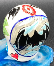 Load image into Gallery viewer, Inspired by nature, this ceramic skull statuette is full of vibrant color and intricate details. The primary color is white with a batty for bats theme and with multi-color floral motifs, along with hearts and leaves and lively colorful accents around the entire skull. Measurements: H 2 3/4” x W 2” x D 2”