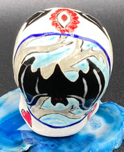 Load image into Gallery viewer, Inspired by nature, this ceramic skull statuette is full of vibrant color and intricate details. The primary color is white with a batty for bats theme and with multi-color floral motifs, along with hearts and leaves and lively colorful accents around the entire skull. Measurements: H 2 3/4” x W 2” x D 2”