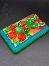 Load image into Gallery viewer, This handcrafted polymer clay wall art features a wood frame painted in a gradient from light yellow to dark red, creating a stunning sunset look. With a bright green skull cactus plant and bright yellow blooming flowers. Boasting vivid marigold blooms and a bright teal and green hue frame to make a bold contrast with the warm background hue. this piece is sure to make a statement. Measurements: