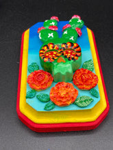 Load image into Gallery viewer, This handcrafted polymer clay wall art features a wood frame painted in a gradient from light to dark blue, creating a stunning starry night sky look. With a bright green skull cactus plant and bright yellow blooming flowers. Boasting vivid marigold blooms and a bright yellow and red hue frame to make a bold contrast with the warm background hue. This piece is sure to make a statement.