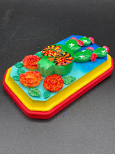 Load image into Gallery viewer, This handcrafted polymer clay wall art features a wood frame painted in a gradient from light to dark blue, creating a stunning starry night sky look. With a bright green skull cactus plant and bright yellow blooming flowers. Boasting vivid marigold blooms and a bright yellow and red hue frame to make a bold contrast with the warm background hue. This piece is sure to make a statement.