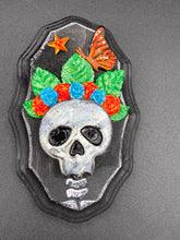 Load image into Gallery viewer, Showcasing a vibrant Frida Kahlo inspired calavera with a dark wood frame, this Day of the Dead wall decor piece is perfect for adding a traditional Mexican folk art touch to any home. Featuring an intricately detailed clay calavera in the style of Frida Kahlo, this Day of the Dead wall art decor is sure to be the centerpiece of any home décor. The calavera is wearing Frida's iconic crown of flowers and a monarch butterfly, ensuring it will bring both a unique and inspiring look to any wall.