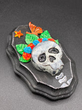 Load image into Gallery viewer, Showcasing a vibrant Frida Kahlo inspired calavera with a dark wood frame, this Day of the Dead wall decor piece is perfect for adding a traditional Mexican folk art touch to any home. Featuring an intricately detailed clay calavera in the style of Frida Kahlo, this Day of the Dead wall art decor is sure to be the centerpiece of any home décor. The calavera is wearing Frida's iconic crown of flowers and a monarch butterfly, ensuring it will bring both a unique and inspiring look to any wall.