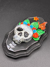 Load image into Gallery viewer, Showcasing a vibrant Frida Kahlo inspired calavera with a dark wood frame, this Day of the Dead wall decor piece is perfect for adding a traditional Mexican folk art touch to any home. Featuring an intricately detailed clay calavera in the style of Frida Kahlo, this Day of the Dead wall art decor is sure to be the centerpiece of any home décor. The calavera is wearing Frida's iconic crown of flowers and a monarch butterfly, ensuring it will bring both a unique and inspiring look to any wall.