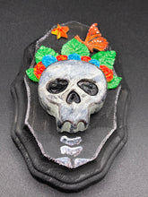 Load image into Gallery viewer, Showcasing a vibrant Frida Kahlo inspired calavera with a dark wood frame, this Day of the Dead wall decor piece is perfect for adding a traditional Mexican folk art touch to any home. Featuring an intricately detailed clay calavera in the style of Frida Kahlo, this Day of the Dead wall art decor is sure to be the centerpiece of any home décor. The calavera is wearing Frida's iconic crown of flowers and a monarch butterfly, ensuring it will bring both a unique and inspiring look to any wall.