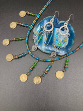 Load image into Gallery viewer, These large chandelier-style earrings feature blues, greens, and iridescent glass beads as well as a finely crafted silver plated leaf charm for added detail. Perfect for bohemian-inspired looks, these versatile earrings can elevate any wardrobe from whimsical hippie to boho chic.  Measurements: 3 1/4” in length