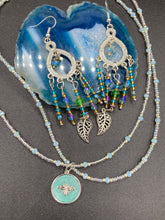 Load image into Gallery viewer, These large chandelier-style earrings feature blues, greens, and iridescent glass beads as well as a finely crafted silver plated leaf charm for added detail. Perfect for bohemian-inspired looks, these versatile earrings can elevate any wardrobe from whimsical hippie to boho chic. Measurements: 3 1/4” in length