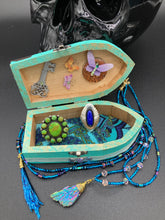 Load image into Gallery viewer, This Whimsical Fairy Wood Coffin Box is a truly unique and magical piece of home decor. With its vibrant turquoise exterior and eye-catching mini door knob, this Steampunk-inspired box is sure to be a conversation starter. Inside, the glittery gold interior and colorful butterfly detailing will bring a touch of fantasy to any room. The silver key and accompanying iridescent crystals complete the mystical and pastel goth look!