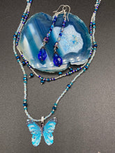 Load image into Gallery viewer, This stunning, one of a kind pair of celestial beaded earrings is a bold addition to any jewelry collection. Crafted with vibrant blue glass beads, the color contains varied shades of blue, purple, and hints of gold to create unique texture. The design is inspired by the awe-inspiring beauty of the majestic galaxy.    Measurements: 2 3/4” in length
