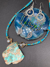 Load image into Gallery viewer, These large chandelier-style earrings feature blues, greens, and iridescent glass beads as well as a finely crafted silver plated leaf charm for added detail. Perfect for bohemian-inspired looks, these versatile earrings can elevate any wardrobe from whimsical hippie to boho chic. Measurements: 3 1/4” in length