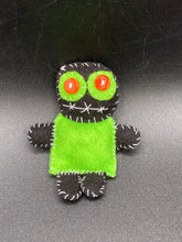 Load image into Gallery viewer, Tiny black and lime green Voodoo Doll stands at 3" in height. He has a lime green torso but the rest is black. He has a tiny round head with tiny orange buttons for eyes which makes him look cute. His mouth is sowed shut of course so good luck trying to talk to him.