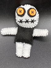 Load image into Gallery viewer, Black and white Voodoo Doll stand at 3 3/4" in height. He has a black torso with white arms and legs, and a big round white head. Bulging yellow/orange buttons for eye and his mouth is sowed shut but despite that he kinda looks like he’s smiling.