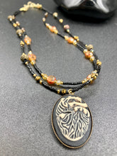 Load image into Gallery viewer, This spooky resin anatomical heart pendant is too cute!!! The pendant is made of resin with brass metal backing. An assortment of floral metal beads to give it a contrast to the soft, dainty style of the glass beaded necklace. Tiny shimmer black glass beads with yellow and orange glass beads to give it a pop of color. Necklace measures 16” adjustable up to 18” in length, pendant is 1 1/4” Height