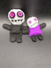 Load image into Gallery viewer, Creepy black and purple Voodoo Doll stands tall at 3 3/8" in height. He’s all black like a shadow but has a round white head. Bright purple buttons for eyes are perfect to see you better with. Mini socially awkward black and purple Voodoo Doll stands at 2 3/4" in height. He has a bright purple torso with black limbs and a large white head and matching purple biddy eyes.