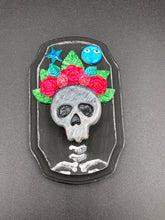 Load image into Gallery viewer, Showcasing a dark theme Frida Kahlo inspired calavera with a dark wood frame, this Day of the Dead wall decor piece is perfect for adding a traditional Mexican folk art touch to any home. Featuring an intricately detailed clay calavera in the style of Frida Kahlo, this Day of the Dead wall art decor is sure to be the centerpiece of any home décor. The calavera is wearing Frida's iconic crown of flowers, ensuring it will bring both a unique and inspiring look to any wall.