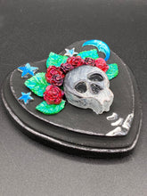 Load image into Gallery viewer, Showcasing a dark theme Frida Kahlo inspired calavera with a dark wood frame, this Day of the Dead wall decor piece is perfect for adding a traditional Mexican folk art touch to any home. Featuring an intricately detailed clay calavera in the style of Frida Kahlo, this Day of the Dead wall art decor is sure to be the centerpiece of any home décor. The calavera is wearing Frida's iconic crown of flowers, ensuring it will bring both a unique and inspiring look to any wall.