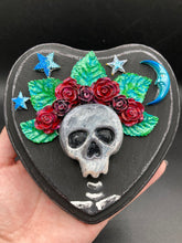 Load image into Gallery viewer, Showcasing a dark theme Frida Kahlo inspired calavera with a dark wood frame, this Day of the Dead wall decor piece is perfect for adding a traditional Mexican folk art touch to any home. Featuring an intricately detailed clay calavera in the style of Frida Kahlo, this Day of the Dead wall art decor is sure to be the centerpiece of any home décor. The calavera is wearing Frida's iconic crown of flowers, ensuring it will bring both a unique and inspiring look to any wall.