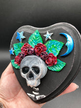 Load image into Gallery viewer, Showcasing a dark theme Frida Kahlo inspired calavera with a dark wood frame, this Day of the Dead wall decor piece is perfect for adding a traditional Mexican folk art touch to any home. Featuring an intricately detailed clay calavera in the style of Frida Kahlo, this Day of the Dead wall art decor is sure to be the centerpiece of any home décor. The calavera is wearing Frida's iconic crown of flowers, ensuring it will bring both a unique and inspiring look to any wall.