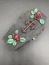 Load image into Gallery viewer, Keep your special jewelry safe in this vintage-inspired wooden coffin jewelry box. Crafted with attention to detail, the box features a black and red cross design, surrounded by dark red roses and a black glittery ribbon. The interior is adorned with a black and silver cross and a bright red crystal in the center. A stylish and secure way to store your beloved accessories.