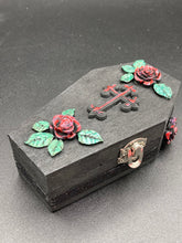 Load image into Gallery viewer, Keep your special jewelry safe in this vintage-inspired wooden coffin jewelry box. Crafted with attention to detail, the box features a black and red cross design, surrounded by dark red roses and a black glittery ribbon. The interior is adorned with a black and silver cross and a bright red crystal in the center. A stylish and secure way to store your beloved accessories.