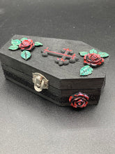 Load image into Gallery viewer, Keep your special jewelry safe in this vintage-inspired wooden coffin jewelry box. Crafted with attention to detail, the box features a black and red cross design, surrounded by dark red roses and a black glittery ribbon. The interior is adorned with a black and silver cross and a bright red crystal in the center. A stylish and secure way to store your beloved accessories.