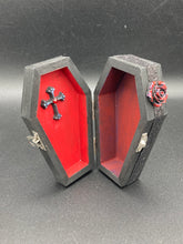 Load image into Gallery viewer, Keep your special jewelry safe in this vintage-inspired wooden coffin jewelry box. Crafted with attention to detail, the box features a black and red cross design, surrounded by dark red roses and a black glittery ribbon. The interior is adorned with a black and silver cross and a bright red crystal in the center. A stylish and secure way to store your beloved accessories.