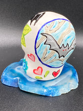 Load image into Gallery viewer, This mini ceramic sugar skull is an intricate piece of art, inspired by nature and drenched in vibrant colors and details. Featuring a white base and multi-colored floral motifs, notable features include hearts and leaves as well as lively accents that encircle the skull. A beautiful Dia De Los Muertos or Day of the Dead-themed decoration. Measurements: H 2 3/4” x W 2” x D 2”