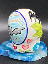 Load image into Gallery viewer, This mini ceramic sugar skull is an intricate piece of art, inspired by nature and drenched in vibrant colors and details. Featuring a white base and multi-colored floral motifs, notable features include hearts and leaves as well as lively accents that encircle the skull. A beautiful Dia De Los Muertos or Day of the Dead-themed decoration. Measurements: H 2 3/4” x W 2” x D 2”