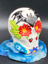 Load image into Gallery viewer, This mini ceramic sugar skull is an intricate piece of art, inspired by nature and drenched in vibrant colors and details. Featuring a white base and multi-colored floral motifs, notable features include hearts and leaves as well as lively accents that encircle the skull. A beautiful Dia De Los Muertos or Day of the Dead-themed decoration. Measurements: H 2 3/4” x W 2” x D 2”