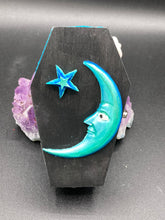 Load image into Gallery viewer, This sleek black box has an eye-catching turquoise crescent at its center, accompanied by a bright blue ribbon and a dainty white moon. Inside, the interior is decorated with a vivid royal blue and detailed with a small crescent moon and black-and-silver cross. Coffin Dimensions: Length: 4 1/2 Inches; Width: 2 1/2 inches; Height: 1 5/8 Inches