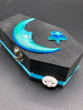 Load image into Gallery viewer, This sleek black box has an eye-catching turquoise crescent at its center, accompanied by a bright blue ribbon and a dainty white moon. Inside, the interior is decorated with a vivid royal blue and detailed with a small crescent moon and black-and-silver cross. Coffin Dimensions: Length: 4 1/2 Inches; Width: 2 1/2 inches; Height: 1 5/8 Inches