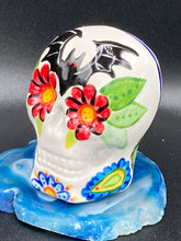 Load image into Gallery viewer, This Bat Lovers Ceramic Skull Art is a unique addition to any dark gothic collection. Featuring a mini batty with bright red eyes and outlined in royal blue, accented with white lines to highlight its small bones and an additional bat with vibrant red eyes on the opposite side. Enjoy the playful contrast of warm tones and a darker theme in this eye-catching figurine. Measurements: H 2 3/4” x W 2” x D 2”