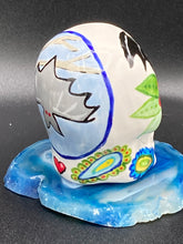 Load image into Gallery viewer, Inspired by nature, this ceramic skull statuette is full of vibrant color and intricate details. The primary color is white with a batty for bats theme and with multi-color floral motifs, along with hearts and leaves and lively colorful accents around the entire skull. Measurements: H 2 3/4” x W 2” x D 2”