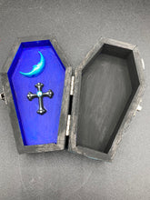 Load image into Gallery viewer, This sleek black box has an eye-catching turquoise crescent at its center, accompanied by a bright blue ribbon and a dainty white moon. Inside, the interior is decorated with a vivid royal blue and detailed with a small crescent moon and black-and-silver cross. Coffin Dimensions: Length: 4 1/2 Inches; Width: 2 1/2 inches; Height: 1 5/8 Inches