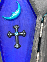 Load image into Gallery viewer, This sleek black box has an eye-catching turquoise crescent at its center, accompanied by a bright blue ribbon and a dainty white moon. Inside, the interior is decorated with a vivid royal blue and detailed with a small crescent moon and black-and-silver cross. Coffin Dimensions: Length: 4 1/2 Inches; Width: 2 1/2 inches; Height: 1 5/8 Inches